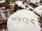 Handwriting of the word winter on a block of wood after first snow from close-up side angle