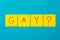 Handwritten black inscription gay with question mark on yellow square stickers on a blue background close-up, horizontal