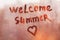 Handwritten text Welcome summer and heart shape ddy wet orange window in city on sunset