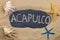 Handwritten word ACAPULCO written in chalk, among seashells and starfishes