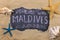 Handwritten word MALDIVES written in chalk, among seashells and starfishes