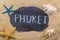 Handwritten word PHUKET written in chalk, among seashells and starfishes