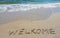 Handwritting inscription welkome word on tropical sandy beach, travel concept card for holidays