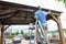 Handyman on a ladder staining a backyard gazebo