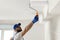 Handyman painting ceiling with white dye, focus on roller