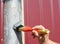 A handyman is painting the metal fence post with a brush applying masking tape, painter`s tape not to spill the paint on the fenc