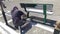 Handyman paints a bench in green color in the village square. The worker paints the bottom bench, her legs