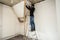 Handyman standing on a ladder and renovating a home, using tools like a hammer