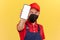 Handyman in uniform and hygienic protective mask showing empty display smartphone at camera, repairman calling online application