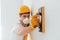 Handyman in yellow uniform and protective mask polishing wall indoors. House renovation conception