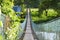 Hanging bridge full of green bushes and made of chain link fence and of plywood for path at rural of Penampang, Sabah, Mal