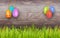 Hanging Easter eggs on rustic background with copy space and border of grass at the bottom. Holiday banner template.