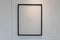 Hanging empty black wooden picture frame on orderly dot or hole wall with orange light form ceiling