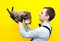 Hansome man in blue shirt and black suspender holding on back brown tabby cat on yellow