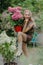 Happily smiling girl holds flower pot with hydrangea in summer garden