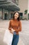 Happiness, consumerism, sale and people concept - smiling young Asian woman with shopping bags at outdoor shopping mall