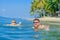 Happiness portrait in tropical water: blond boy lying on the water surface as a crocodile and his brown-haired bearded father