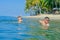 Happiness portrait in tropical water: blond boy lying on the water surface as a crocodile and his brown-haired bearded father