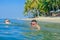 Happiness portrait in tropical water: blond boy lying on the water surface as a crocodile and his father is swimming