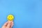 Happiness and positivity concept. Hand holding yellow smiling face in blue background with copy space.