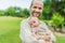 A happy 40-year-old father cradles her newborn in a sun-drenched park. Love, family and generations in harmony