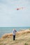 Happy active little child with flying colorful kite standing on sea shore with blue sky during summer leisure vacation activity