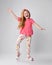 Happy active redhead kid girl in pink t-shirt, colorful pants and sandals stands waving hands, dancing, playing