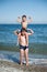 Happy active sport little boy sitting on fat kid shoulders showing strong muscles on summer sea sunny beach during holiday leisure