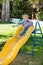 Happy adorable girl on childrens slide on playground near kindergarten Montessori on summer