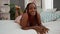 Happy adult african american woman, confident and relaxed, enjoying her lifestyle, lying comfortably smiling on a cozy bed in a