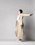 Happy adult woman in beige business casual pantsuit and sneakers stands sideways, dancing. Stylish business female wear