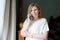 Happy adult woman talking on phone while standing at window against background