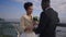 Happy affectionate woman looking with love at man as groom kissing hand of bride standing on bridge outdoors. Portrait