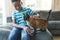 Happy african american boy sitting on couch and petting his cat in sunny living room