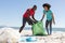 Happy african american couple cleaning sunny beach and collecting litter