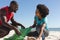 Happy african american couple cleaning sunny beach and collecting litter