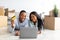 Happy african american couple purchasing house decor in internet store, using laptop and credit card, lying among boxes