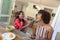 Happy african american daughter feeding mother sitting at table during breakfast and smiling