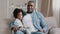 Happy african american family adult father with little funny daughter sitting on sofa in room smiling spending time