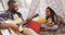 Happy african american father and daughter sitting in blanket tent, playing guitar and singing