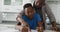 Happy african american father leaning over son sitting at kitchen table helping with his school work