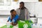 Happy african american father and son in kitchen talking and sorting rubbish for recycling