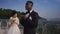 Happy African American groom adjusting wedding suit and bow tie as smiling bride in wedding dress standing at background
