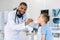 Happy African American male doctor watching patient boy with sore throat in clinic. The doctor examining little boy`s