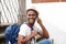 Happy african american male tourist sitting on stairs with bag and talking with cellphone