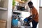 Happy african american man standing in kitchen and unloading dishwasher