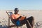 Happy african american man in sunglasses sitting in deckchair reading book on sunny beach