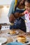 Happy african american mother and daughter pouring honey on pancakes in plate at home