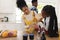 Happy african american mother and daughter pouring pasta to glass jar in kitchen at home, copy space