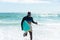 Happy african american senior man carrying surfboard running on shore at beach against sky